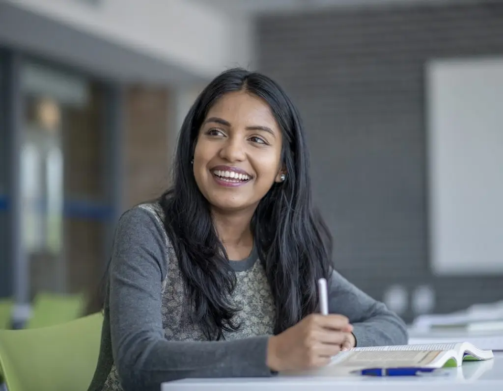A university student smiles across the classroom as she studies.