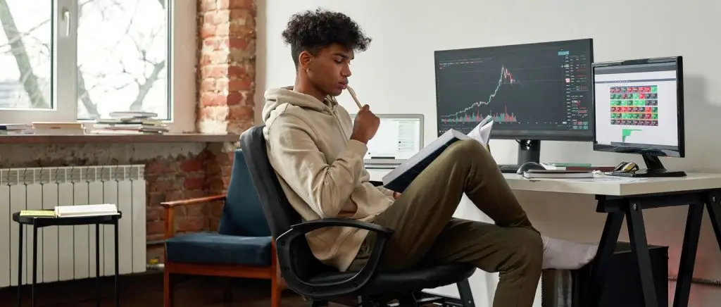 Narrow web banner view of pensive African American millennial gen z male trader read book work online on PC at home. Serious young ethnic man financial expert analyze graph chart. Cryptocurrency.