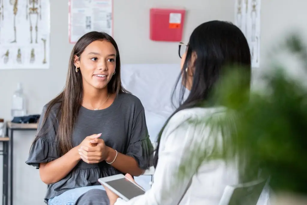 The teenage girl describes her symptoms as the nurse practitioner listens closely.