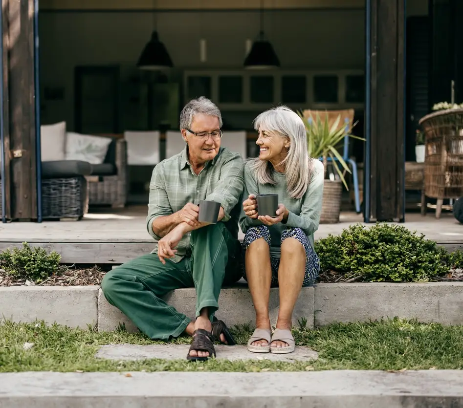 With coffee in hand, a senior couple in their 60s embraces a quiet moment, appreciating the beauty of their home.
